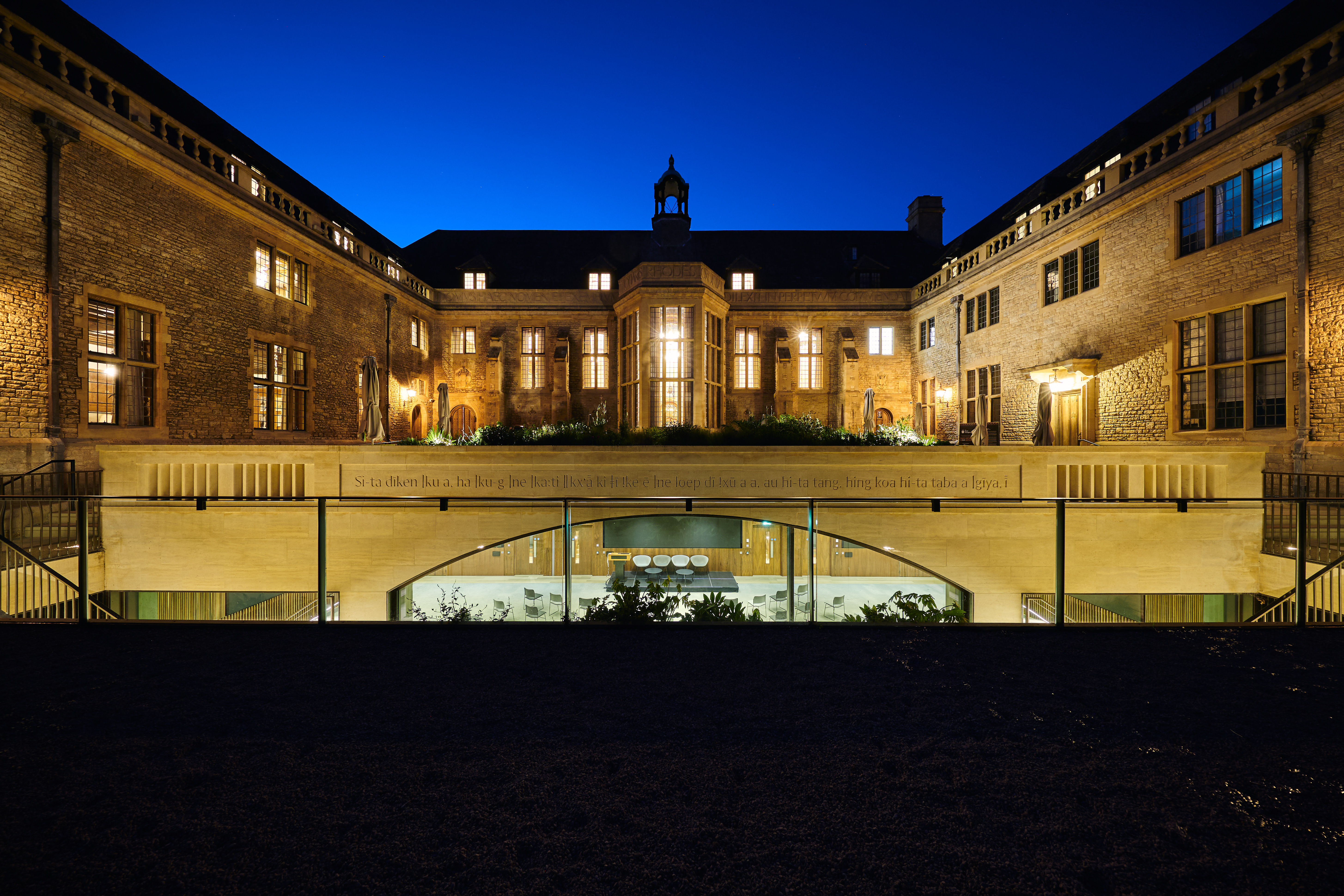 View of the Rhodes House Courtyard at night with lights coming from the windows and the Conference Hall below. 