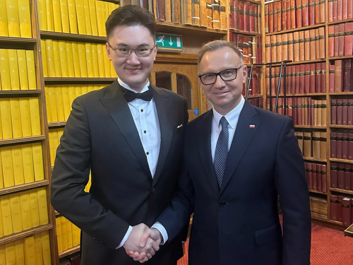 Bincheng Mao and President Andrzej Duda of Poland smile and shake hands in a book-lined study