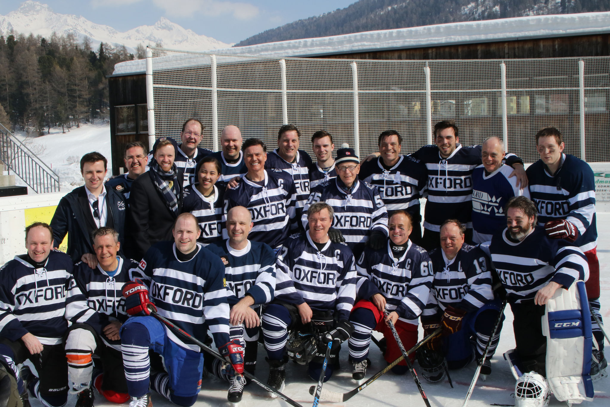Large group all wearing hockey outfits stood on a snowy mountain and posing.