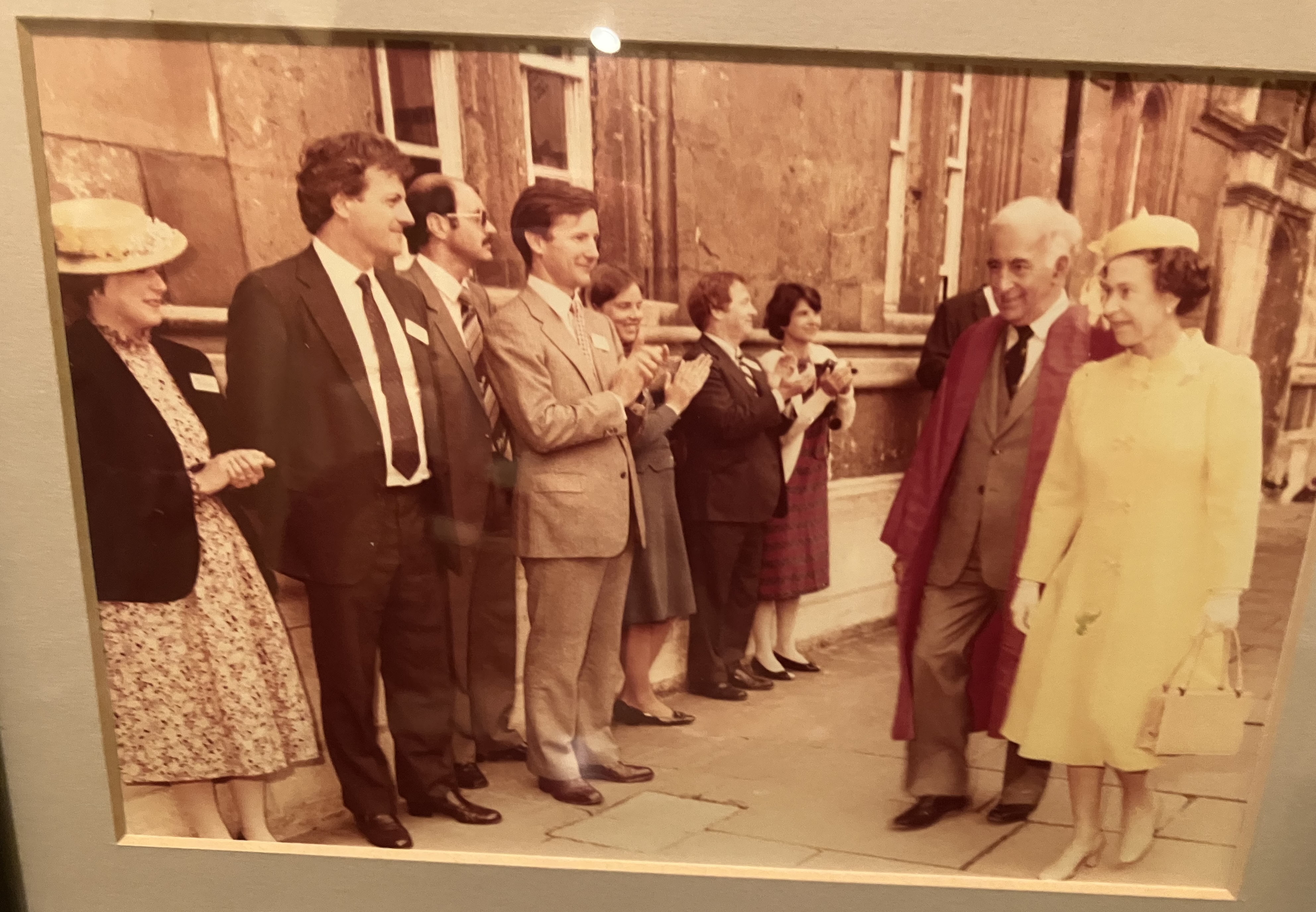 The picture shows Queen Elizabeth II walking on a pavement while a row of people claps, among them Bob