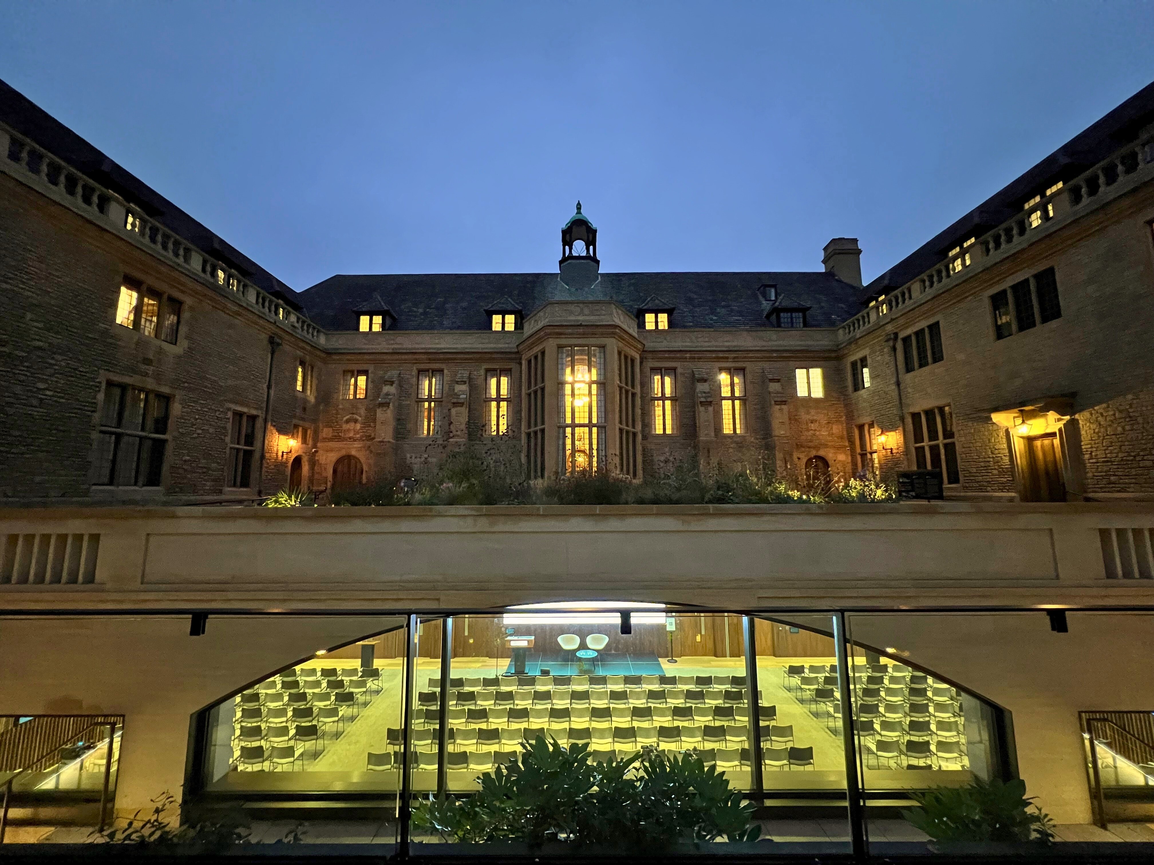 View of the Rhodes House courtyard and Conference Hall at night with windows lit, Hall set up for a conference. 