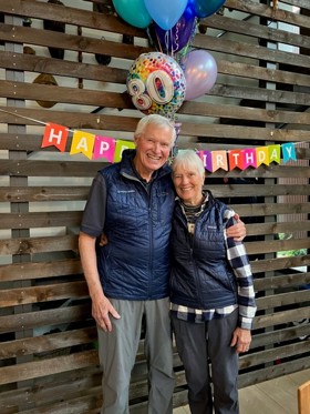 Couple stood smiling in front of happy birthday banner