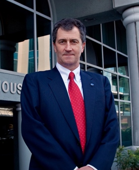 A portrait of John in a navy-blue suit and a red tie