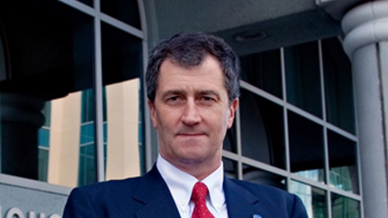 A portrait of John in a navy-blue suit and a red tie