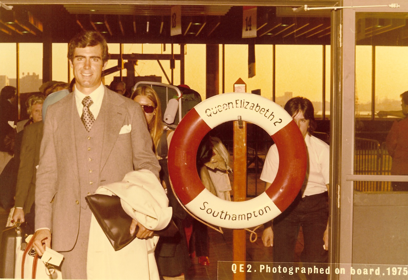 Ken is stood wearing a suit to the left of a life ring that reads 'Queen Elizabeth 2 Southampton'. 
