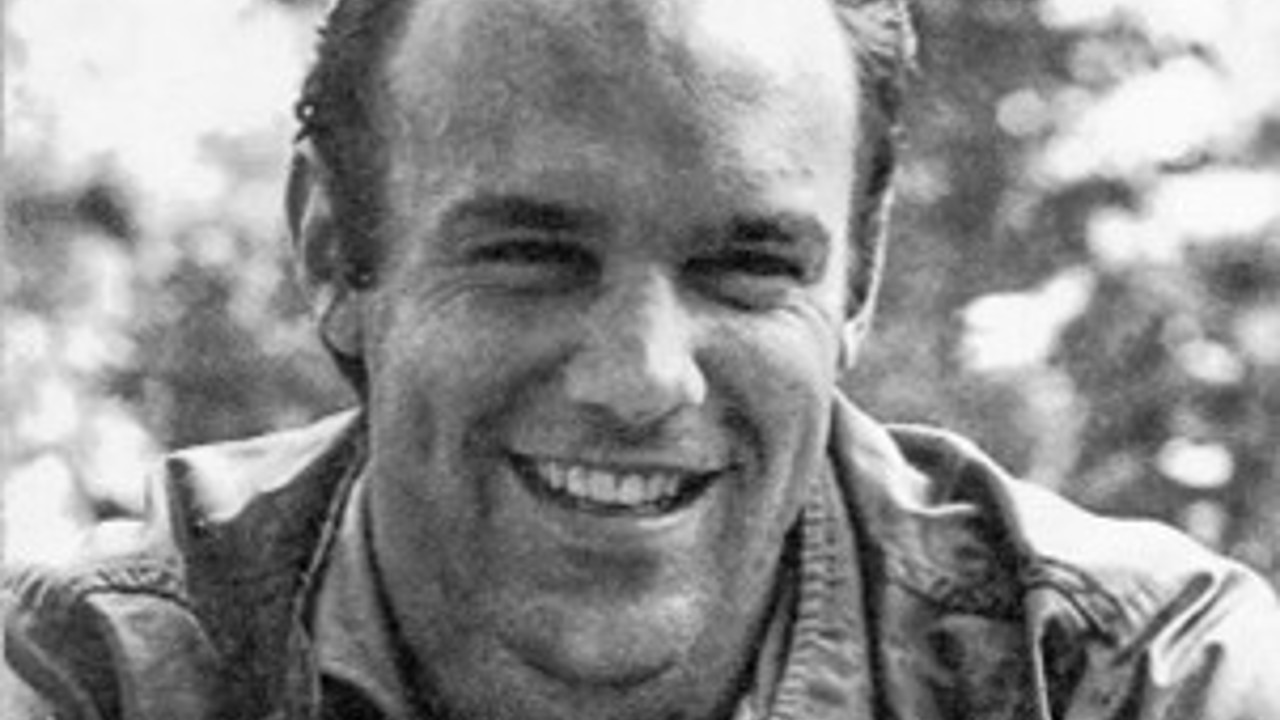 A black-and-white headshot of Peter. He's wearing a thick shirt over a t-shirt. He is smiling and behind him are trees.
