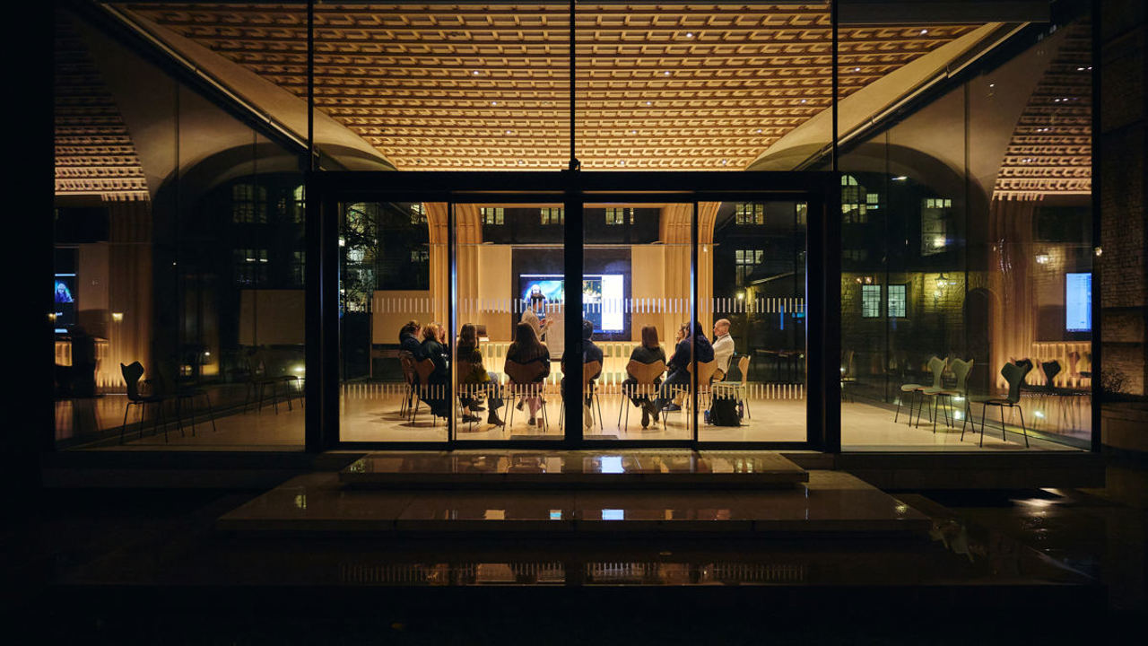 Looking inside the Glass Pavilion at night with delegates in a meeting.