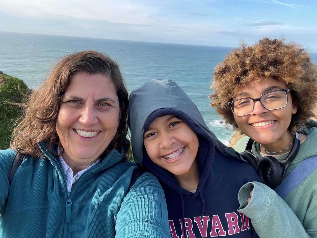 A selfie of Carol and her daughter and son, all smiling with the ocean in the background.
