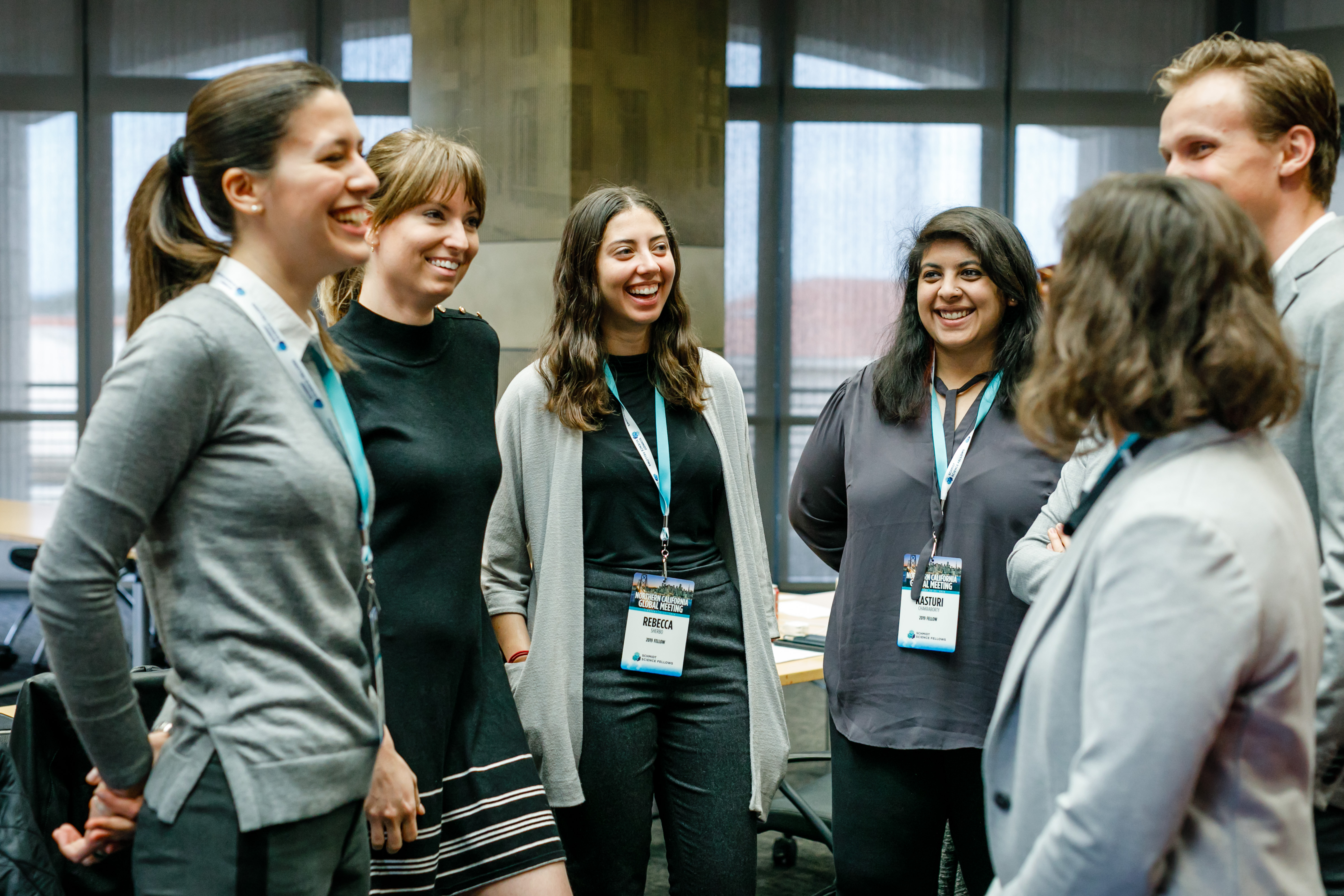 A group of people from the Schmidt Science Fellows programme are standing in a semi-circle, smiling and talking. 