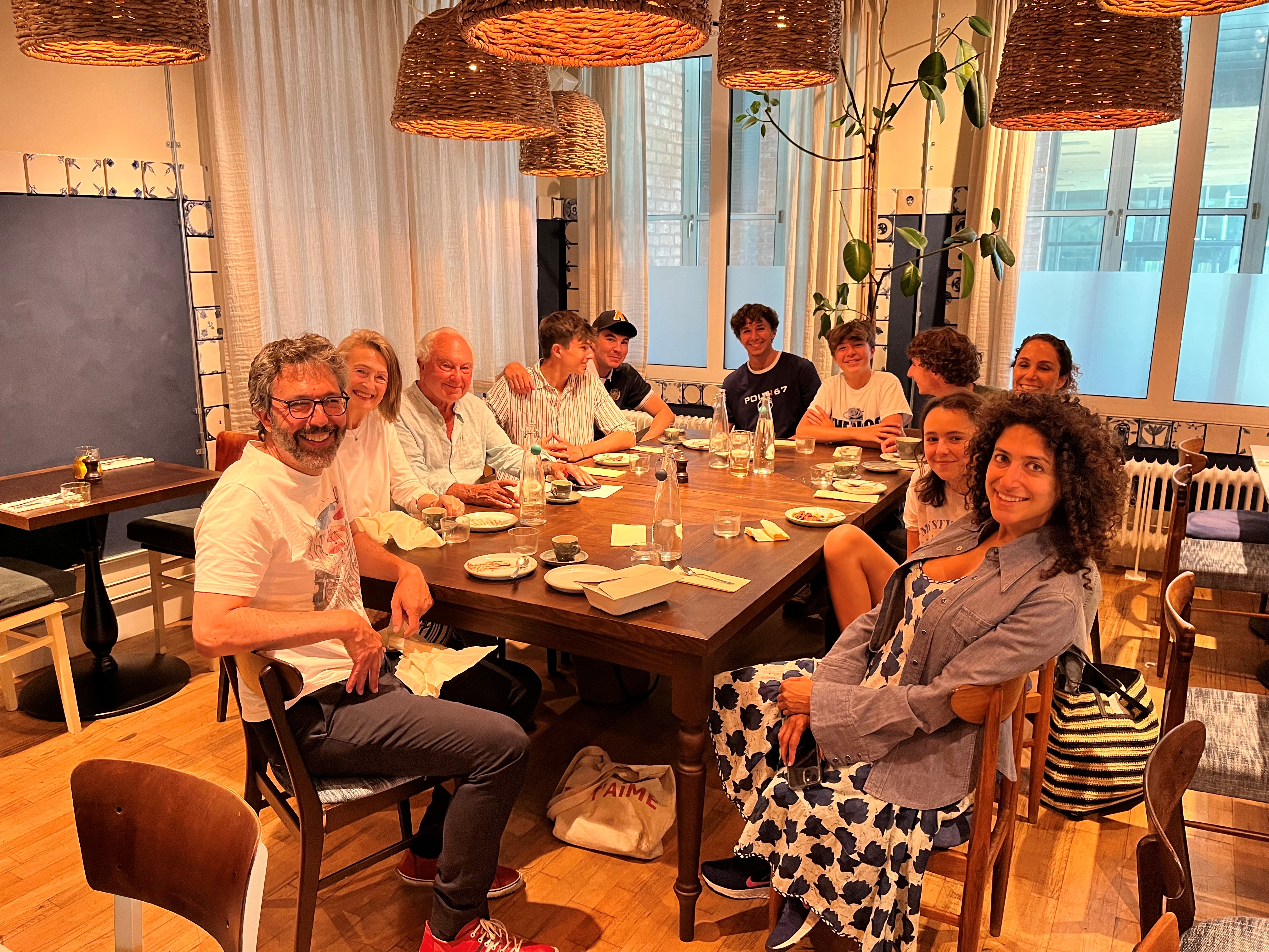 John and his family are sat at a large table, with plates and glasses on it. There are 11 family members in the image.