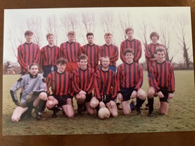 A sports team pose on the playing field in their uniform which is red and navy stripes.