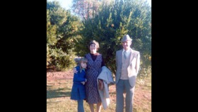 The picture shows a young girl hugging an older woman while an older man in a suit stands next to them