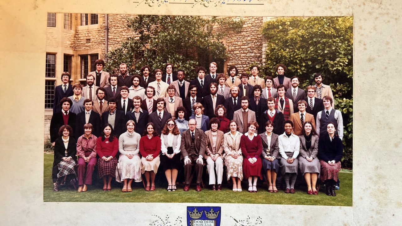 The photo shows a big group of Rhodes Scholars, with trees and buildings in the background