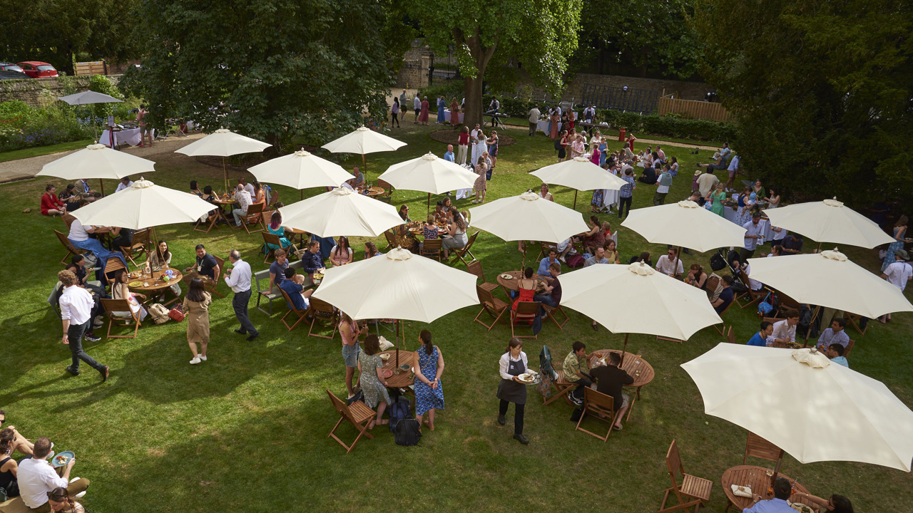 Rhodes House West Lawn with garden party guests and outdoor furniture and umbrellas, as seen from the first floor. Photo courtesy of Nasir Hamid.