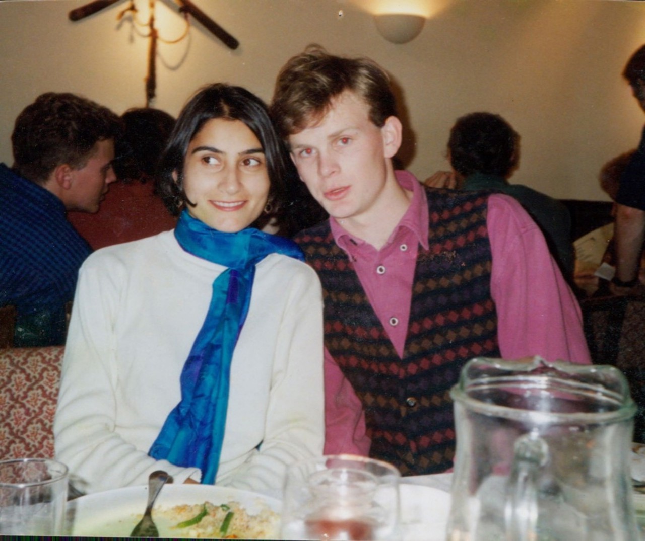 The picture shows Mark sitting with Shazia at a table. Shazia is wearing a white shirt with a blue muffler and Mark is in a pink shirt with a dark cardigan.
