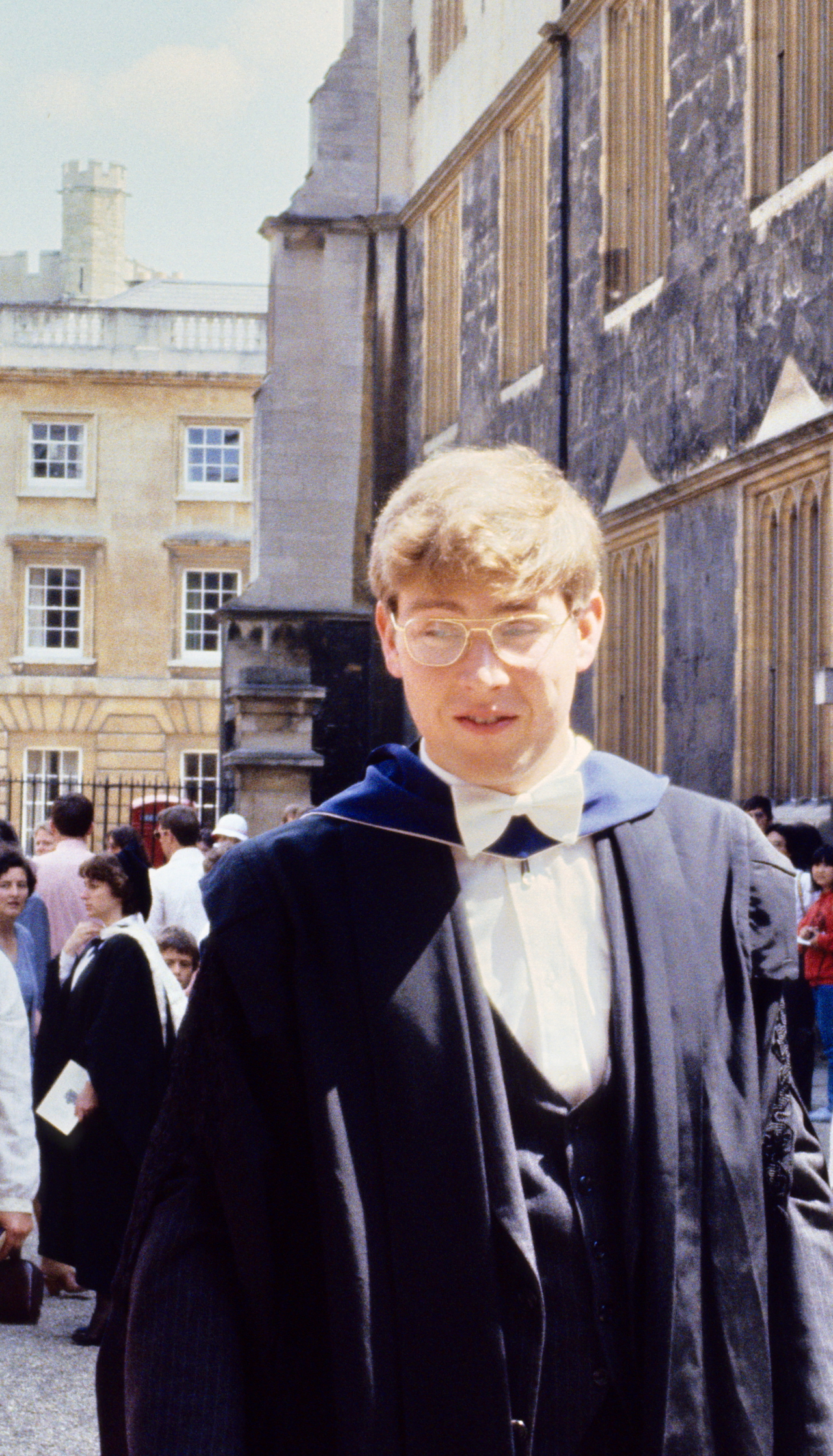 Photo of Chris as a young man in Oxford, wearing a suit and a gown.