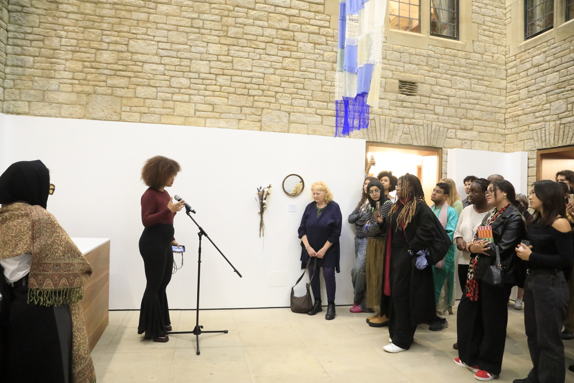Rebecca speaks into a microphone in front of a crowd of attendees, beneath a blue hanging tapestry.
