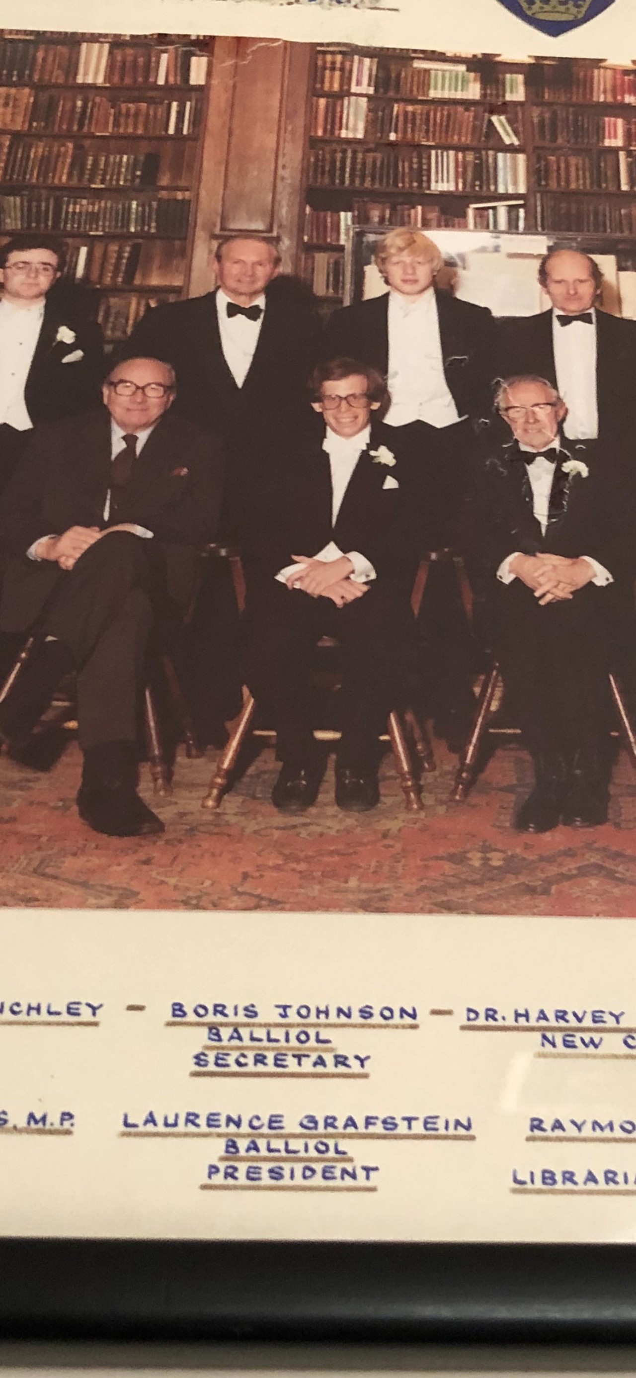 The picture shows members of the Oxford Union with books in the background. They are all in formal attire.