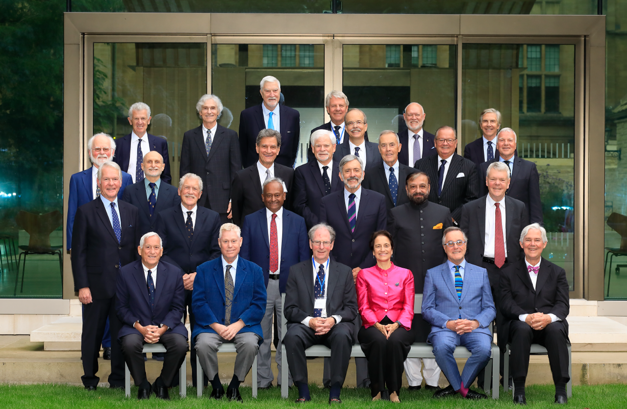Alumni from the Class of 1974 sat in in rows mimicking a school photo with a glass pavillion behind them.
