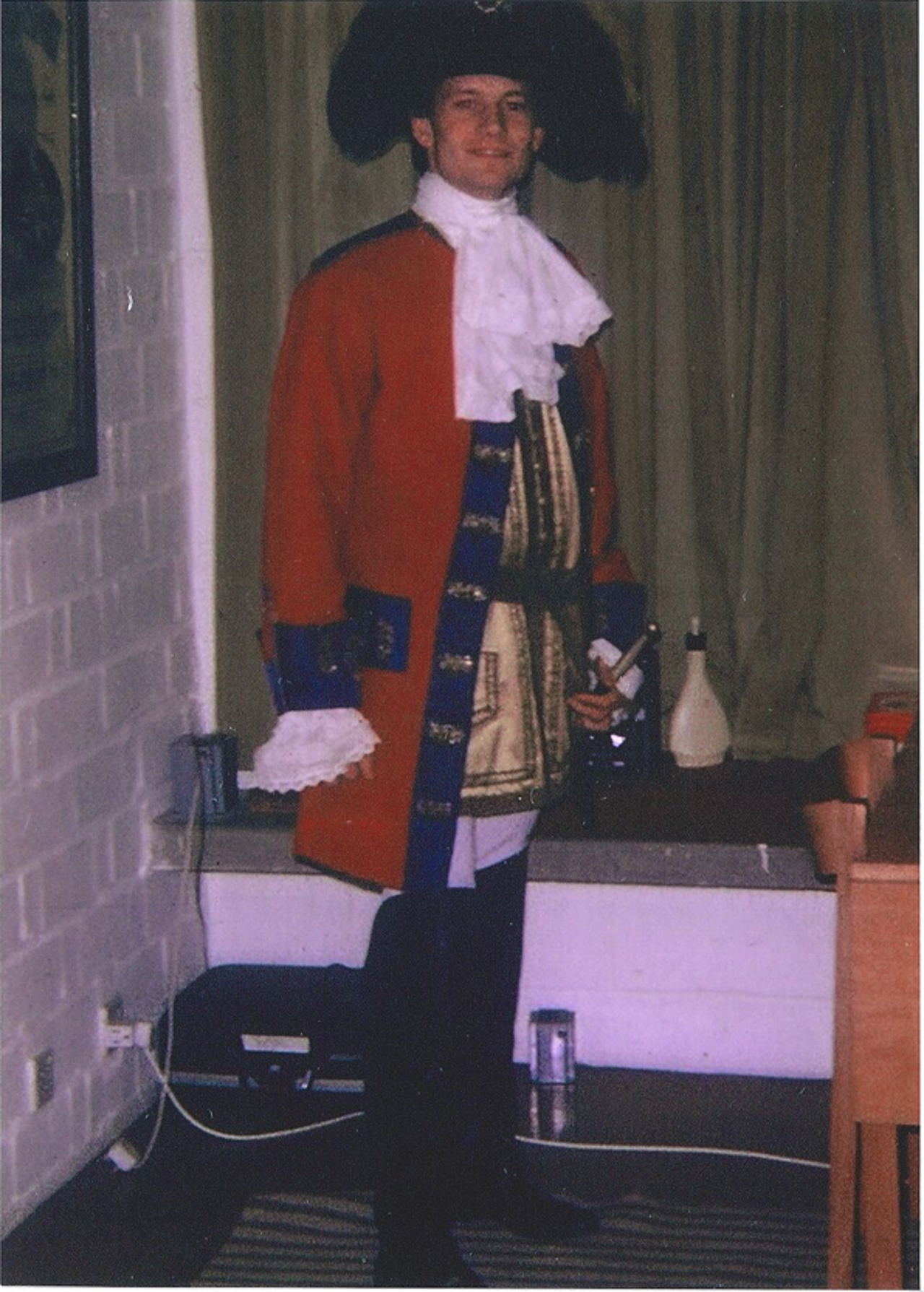 The picture shows Mike in an old military uniform with a red overcoat and a shirt with huge frills,