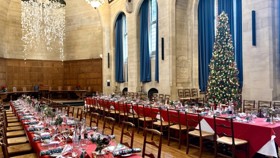 Two long banquet tables in Rhodes House McCall MacBain Hall set for Christmas dinner with a Christmas tree in the bay window