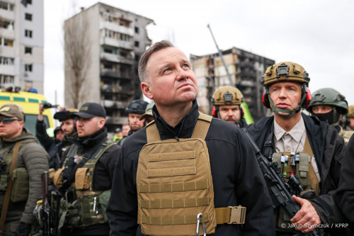 President Duda in a bulletproof vest looks up while standing in front of ruins in Ukraine