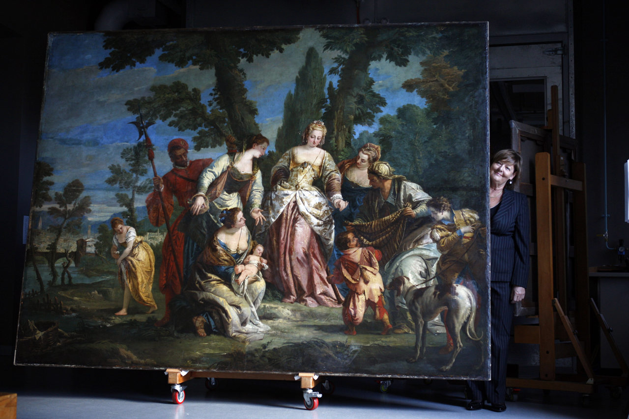 Jaynie stands next to a huge painting depicting the finding of a baby Moses by a group of women.
