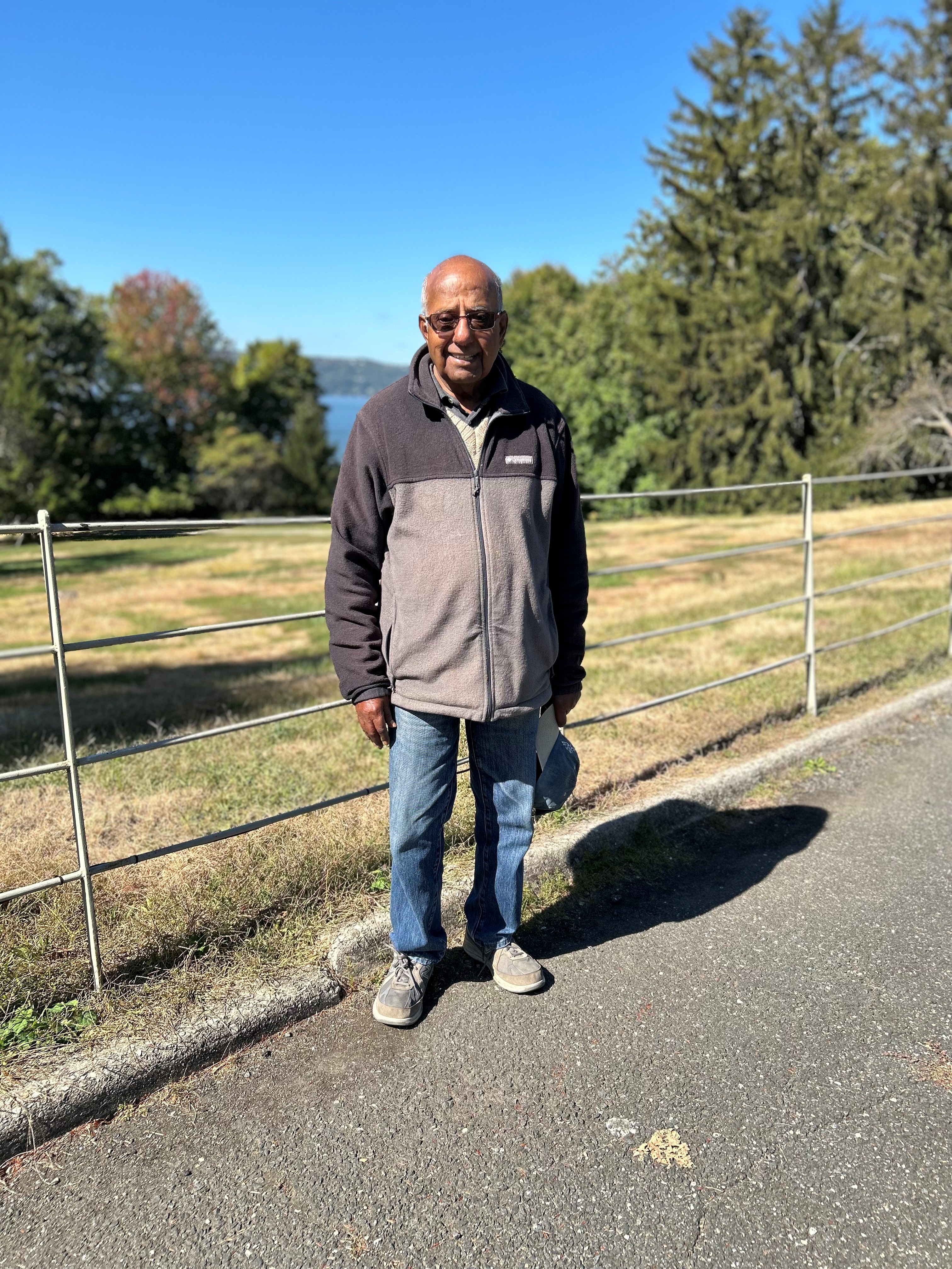 Brij is stood in front of a park view, trees and greenery are seen in the background.