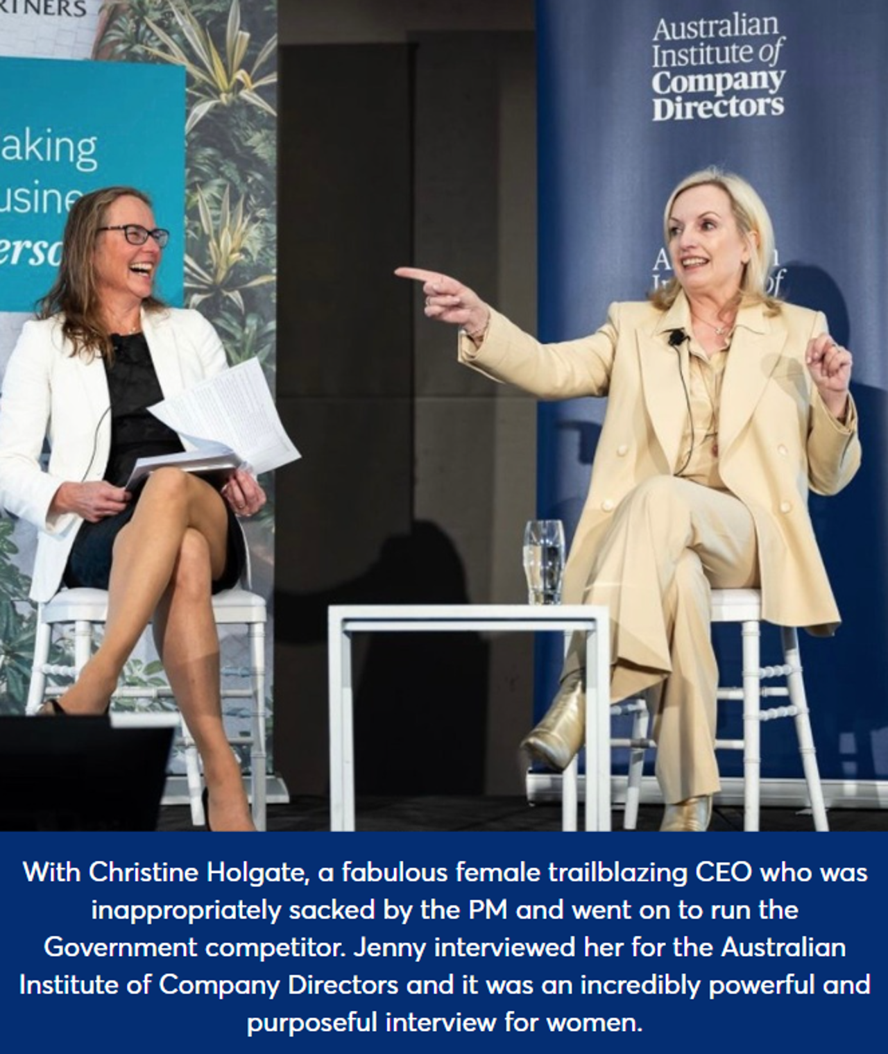 Jenny sat on a chair during a panel discussion, smiling, with Christine Holgate, a fabulous female trailblazing CEO who was inappropriately sacked by the PM and went on to run the Government competitor. Jenny interviewed her for the Australian Institute of Company Directors and it was an incredibly powerful and purposeful interview for women. Both are wearing a suit, and Jen laughs whilst Christine points into the audience.