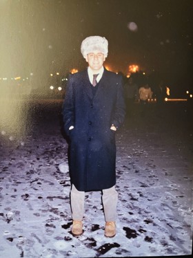 Stood at night in the middle of a snowy street, wearing a furry hat.