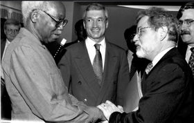 A black-and-white picture showing Richard watching the President shake hands with another man. They are all wearing suits, and smiling.