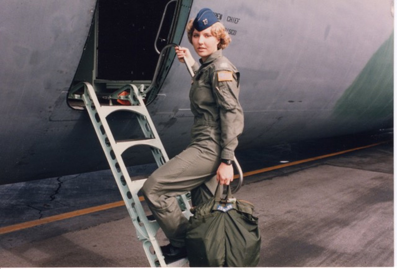 Young Michelle walking up a ladder stepping towards a plane dressed in uniform. She is holding a bag and has turned to look towards the camera.