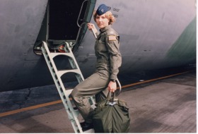 Young Michelle walking up a ladder stepping towards a plane dressed in uniform. She is holding a bag and has turned to look towards the camera.