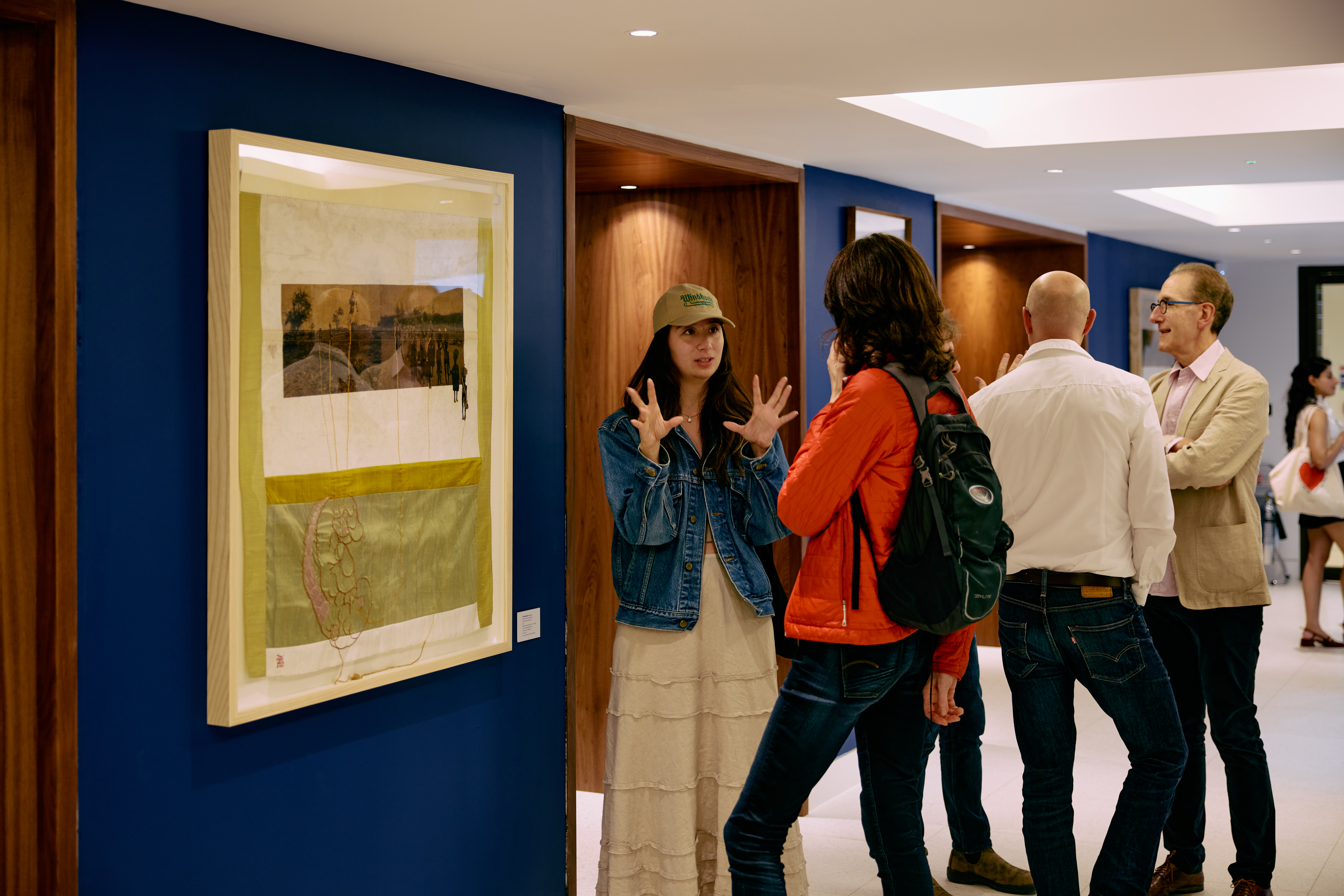 A person standing next to an artwork with an animated gesture, amongst other visitors