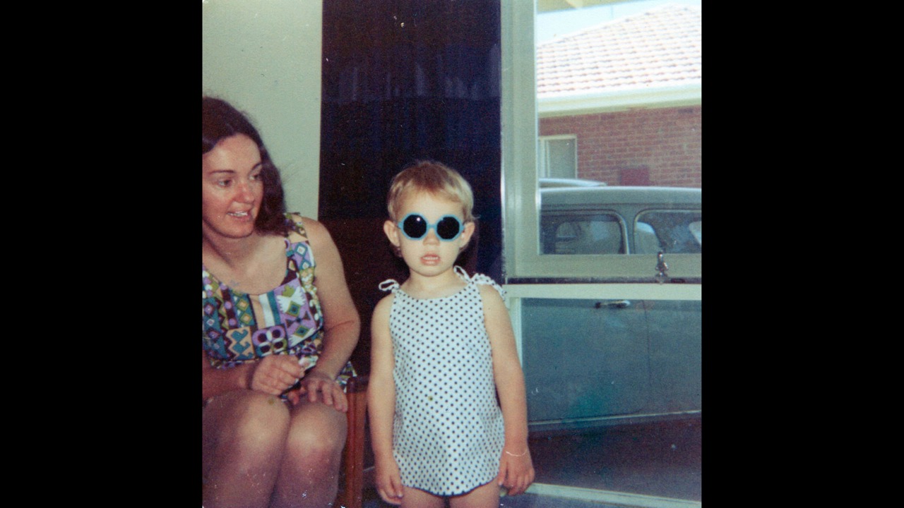 Elle as a child wearing black glasses and standing next to her mother