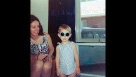Elle as a child wearing black glasses and standing next to her mother
