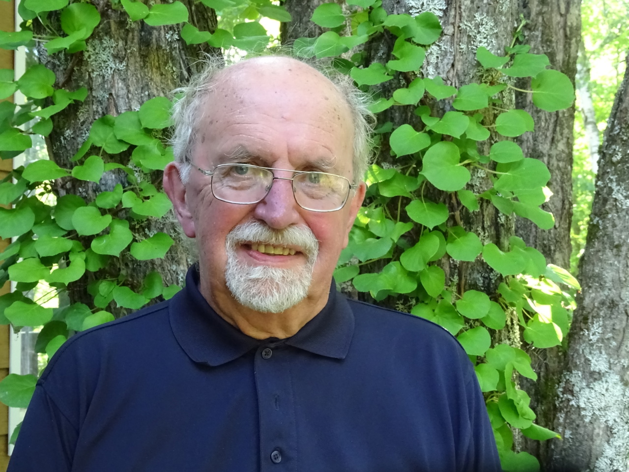 Andrew stood smiling before a leafy tree.