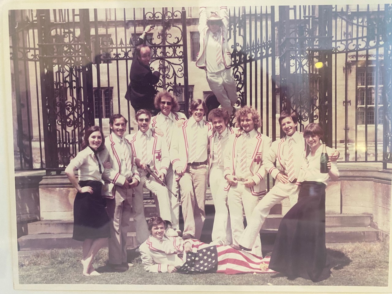 Sepia photo of sports team all stood smiling before a gate, with Nick leaning on the floor holding a USA flag.