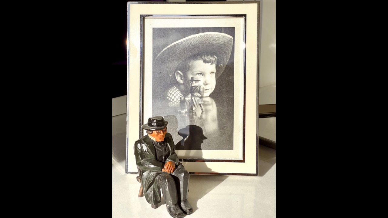 The picture shows a framed black-and-white photo of Eric Redman as a child with a little figurine in front of the frame