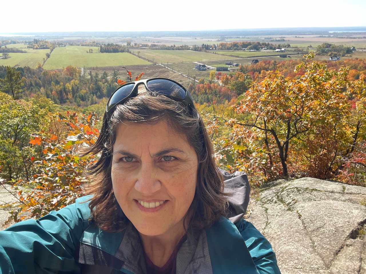 Carol taking a selfie on a hill, smiling, with a field behind her.