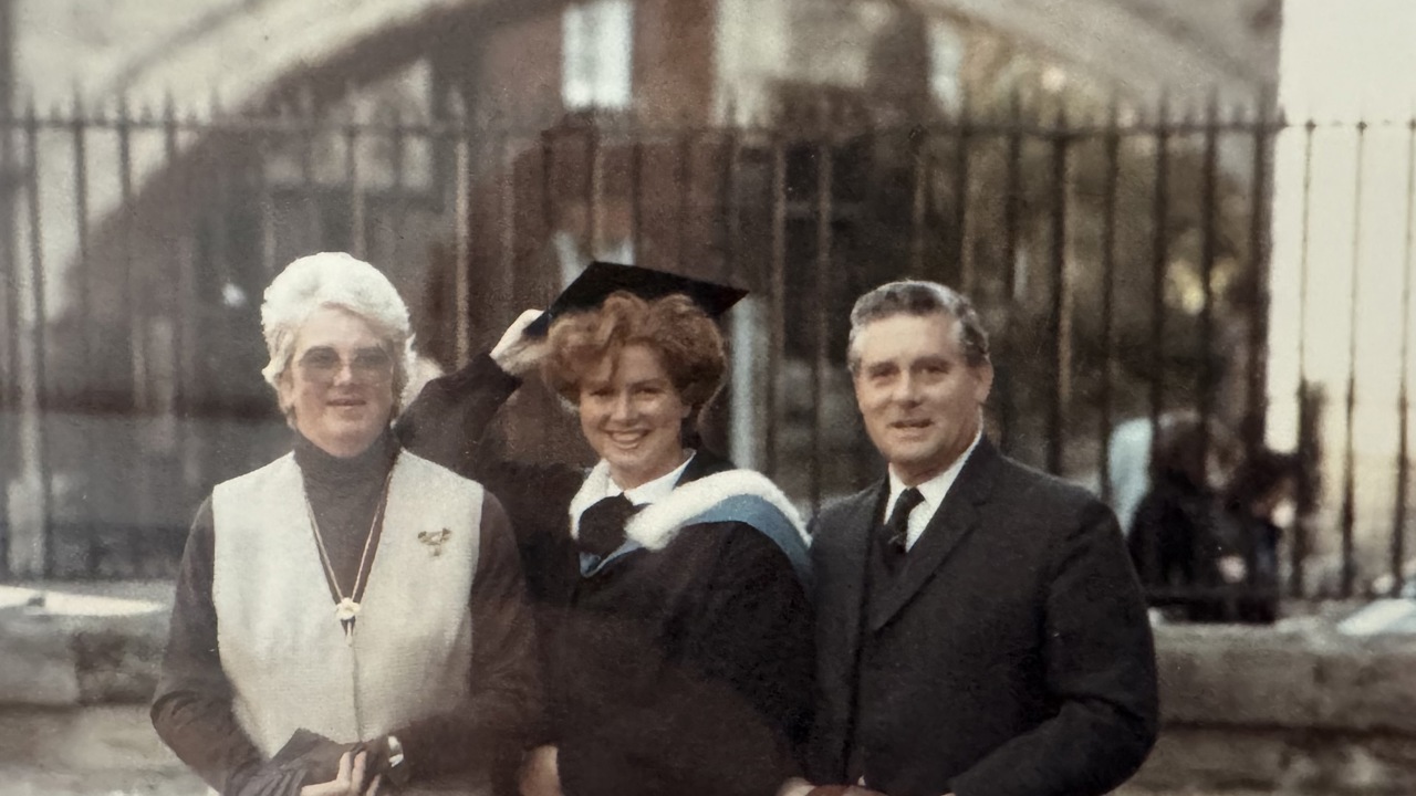 A picture of Elizabeth standing between her parents and wearing a graduation gown