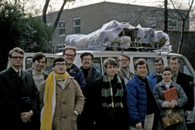 The picture shows a group of people in front of a van. They are all wearing warm clothing.