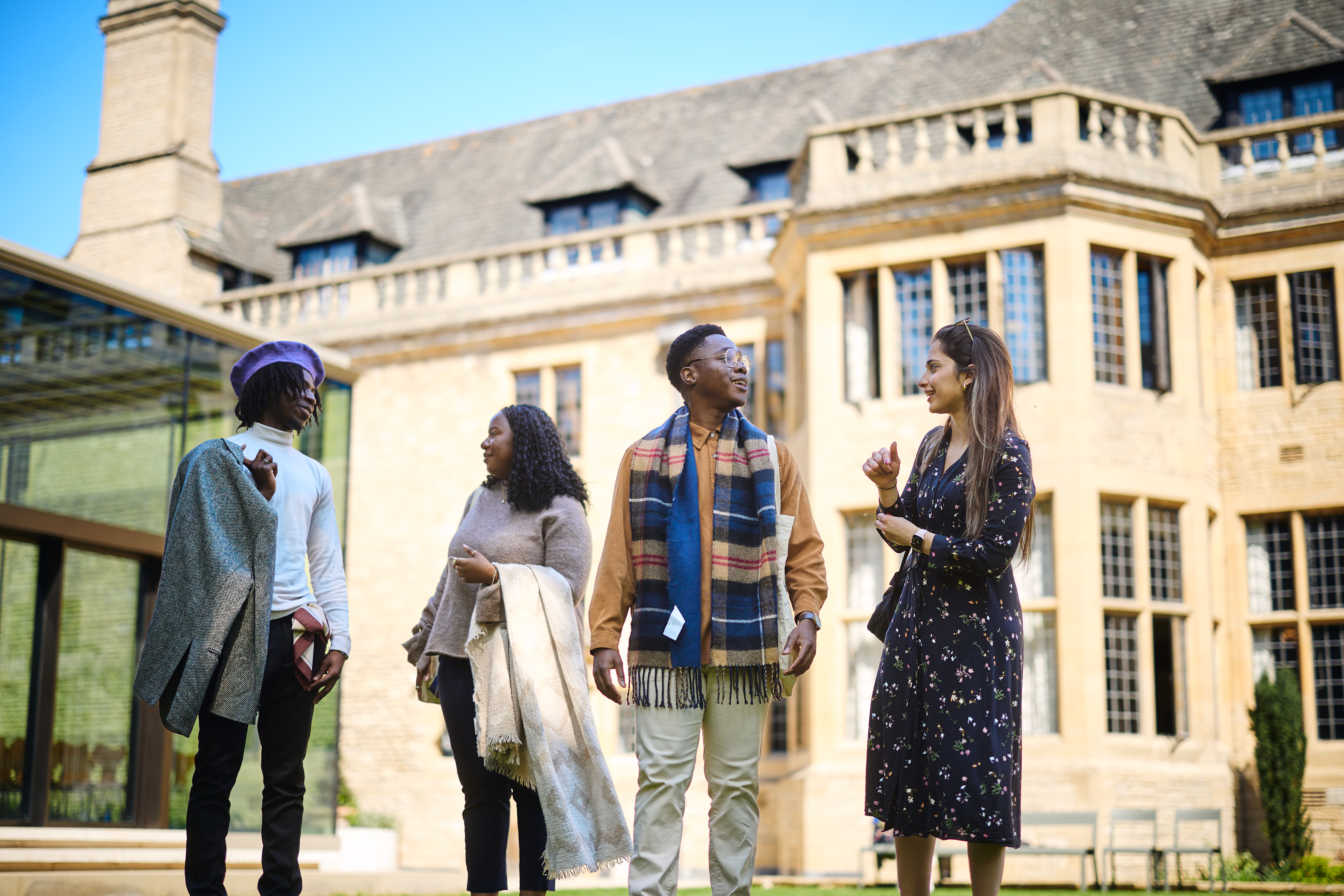 Four Scholars chatting with each other as they walk in front of Rhodes House and the Glass Pavilion.