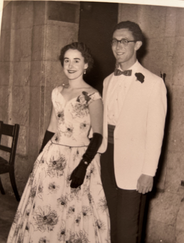 Ken stood in a white blazer and rose to the right of a lady wearing a floral ballgown. Black and white photo