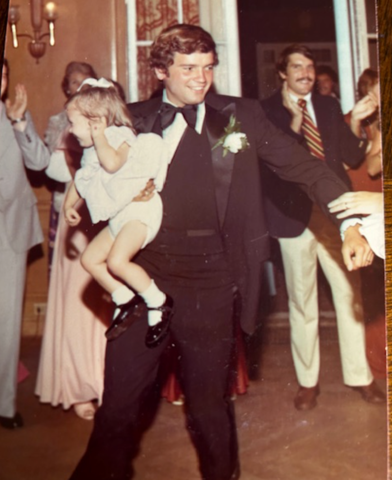 Nick smiling holding a child in his arms, suited, with a crowd behind him.