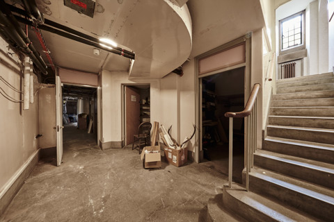 Image of the Rhodes House Basement. There is a stairwell on the right leading to the basement, which is empty and shows a couple of storage boxes in the back.