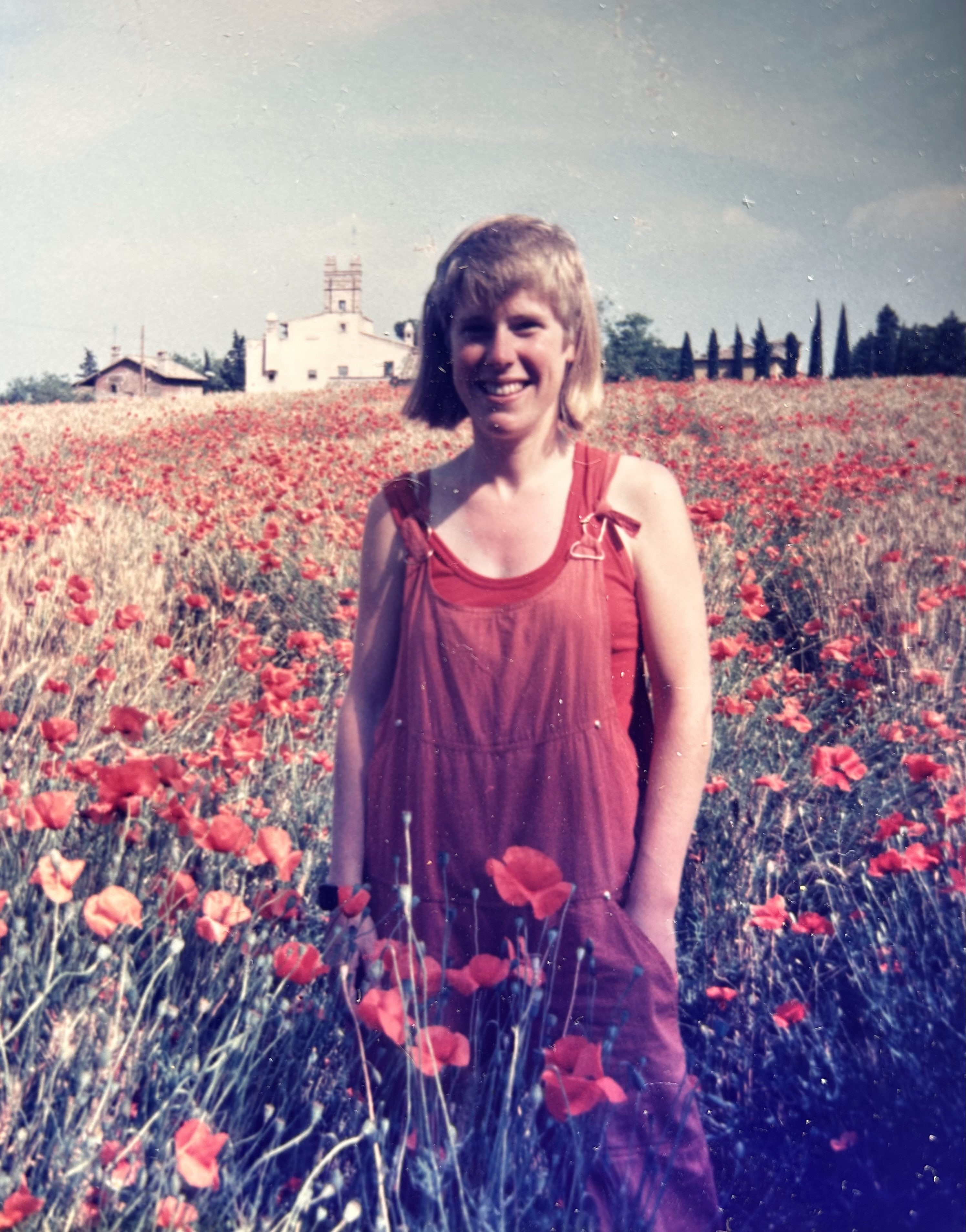 Meredith is stood in red dungarees in the middle of a field of poppies.