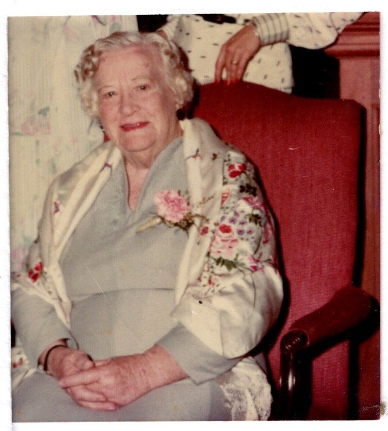 The picture shows an elderly woman in a dress with a floral shawl wrapped around her