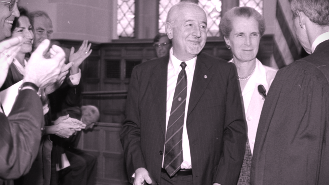 A tinted picture of Guido surrounded by people applauding as he is sworn in