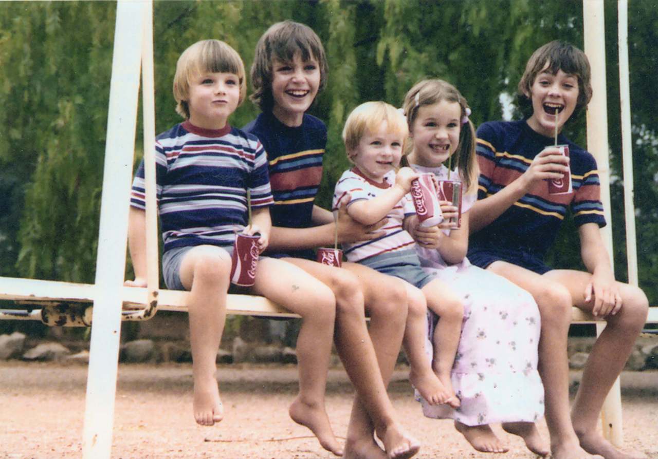 Elle sitting with her brothers (in the darker blue tshirts) and her cousins, all sitting on what looks like a swing